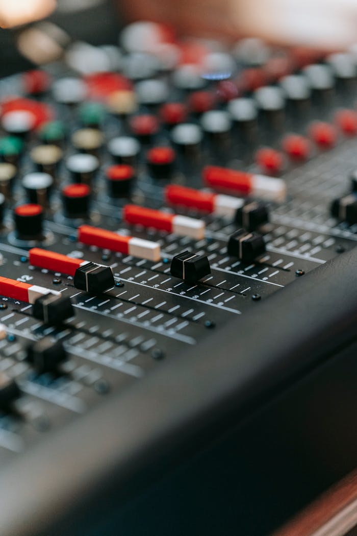 Vertical shot of a professional audio mixer with red potentiometers and switches.